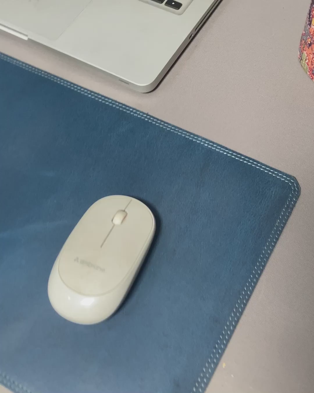 Close-up of a person grasping a blue leather wallet marked "genuine leather" atop a desk mat.