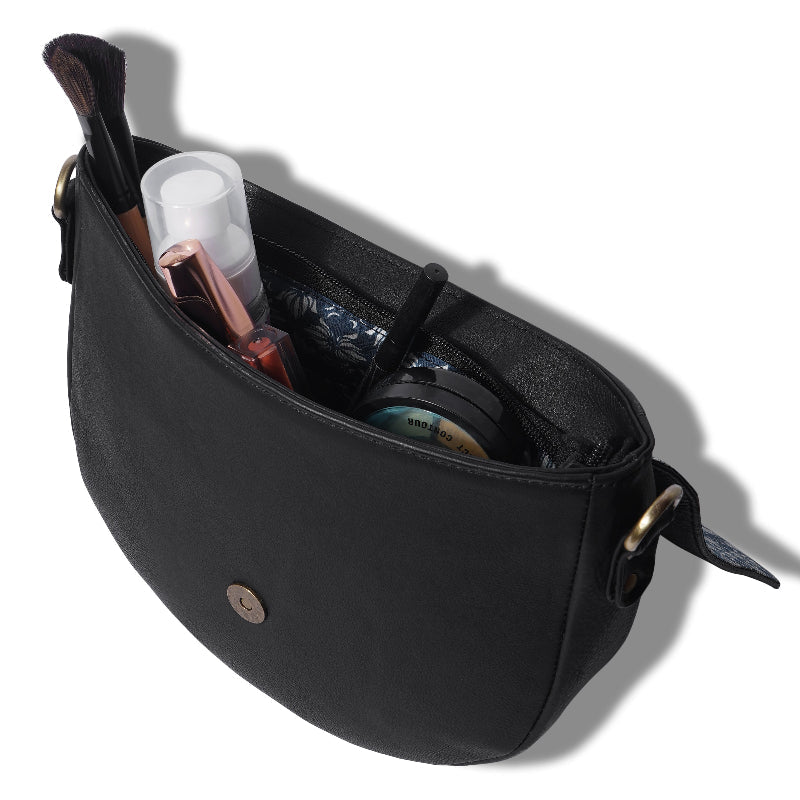 Black crossbody bag with cosmetic items on a white background
