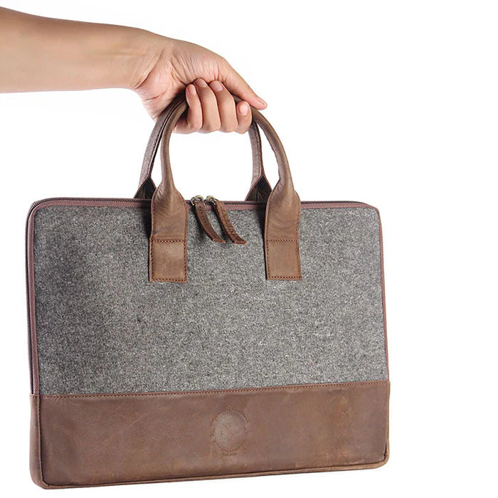 Gray briefcase with brown leather accents held by a hand on a white background