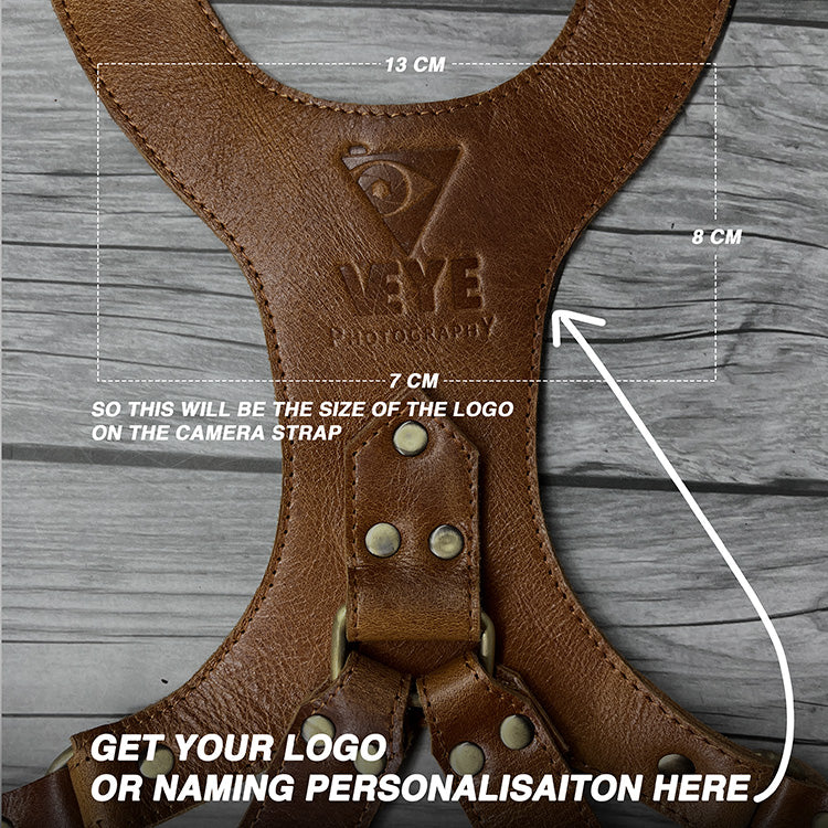 Brown leather camera strap with measurements and branding on a wooden surface
