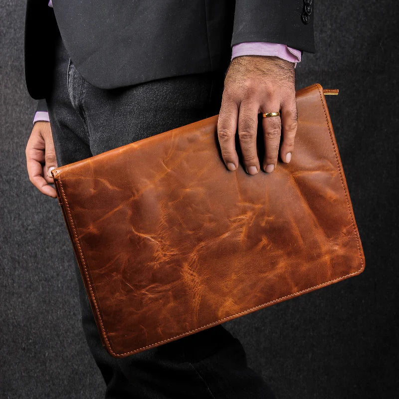 Person holding a brown leather clutch bag against a dark background