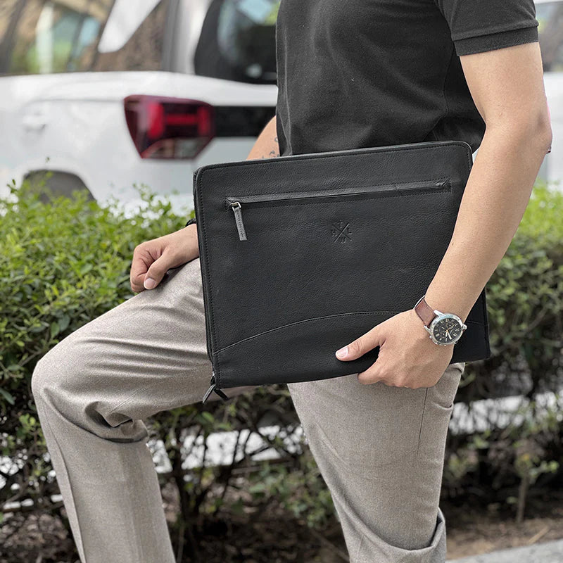 Person holding a black leather clutch bag outdoors with a vehicle in the background