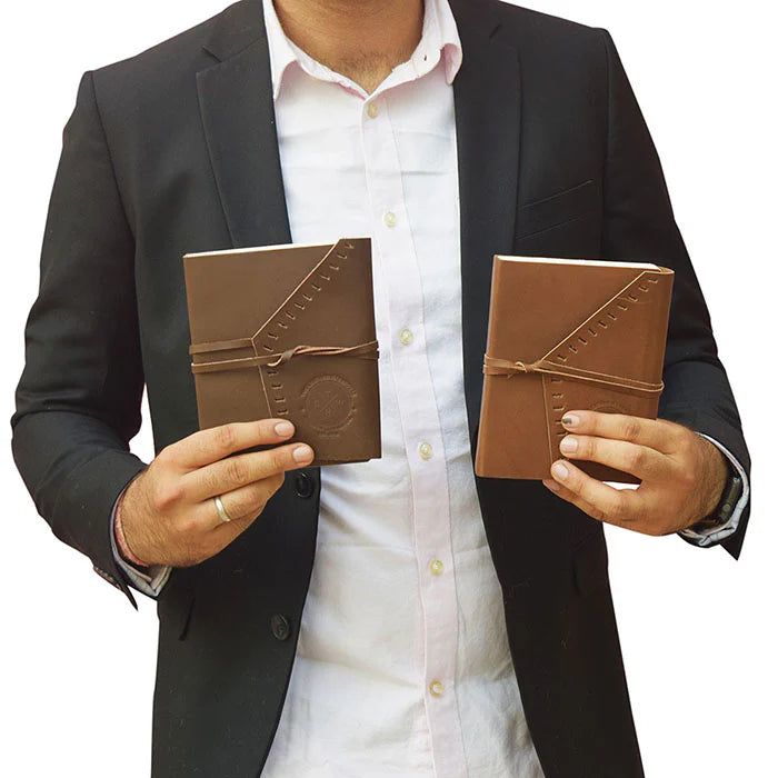 Person holding two brown leather journals against a white background
