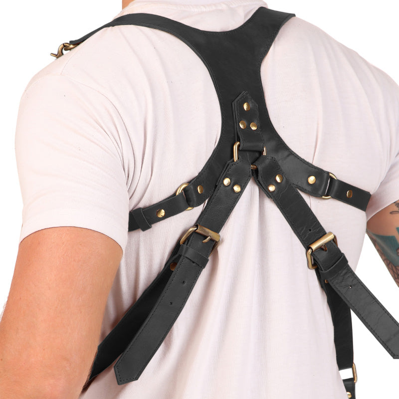 Black leather harness with gold hardware on a person wearing a white t-shirt.