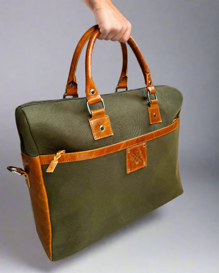 Green bag with brown leather handles and trim held by a hand against a gray background