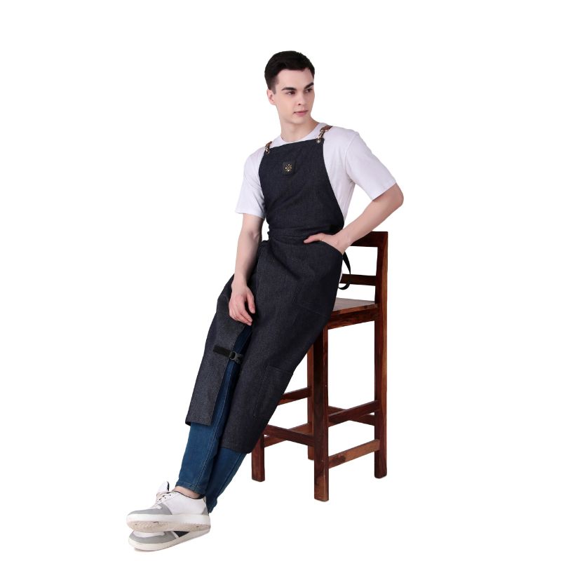 Person wearing a black denim apron sitting on a wooden stool against a white background