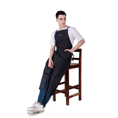 Person wearing a black denim apron sitting on a wooden stool against a white background