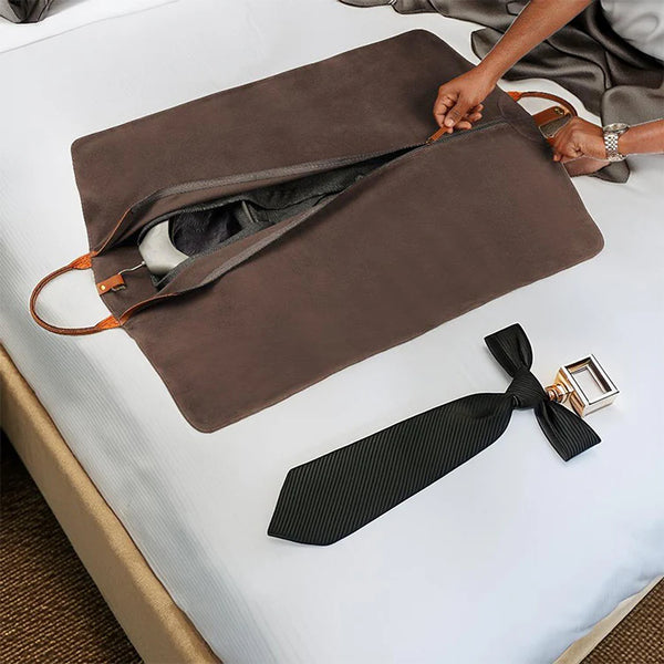 Brown leather travel pouch with a black tie and bow tie on a white surface