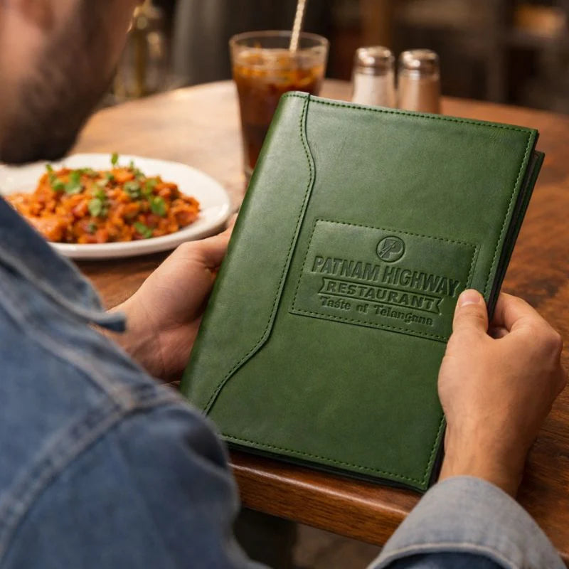 Person holding a green menu from Fatham Highway Restaurant with food and drink in the background.