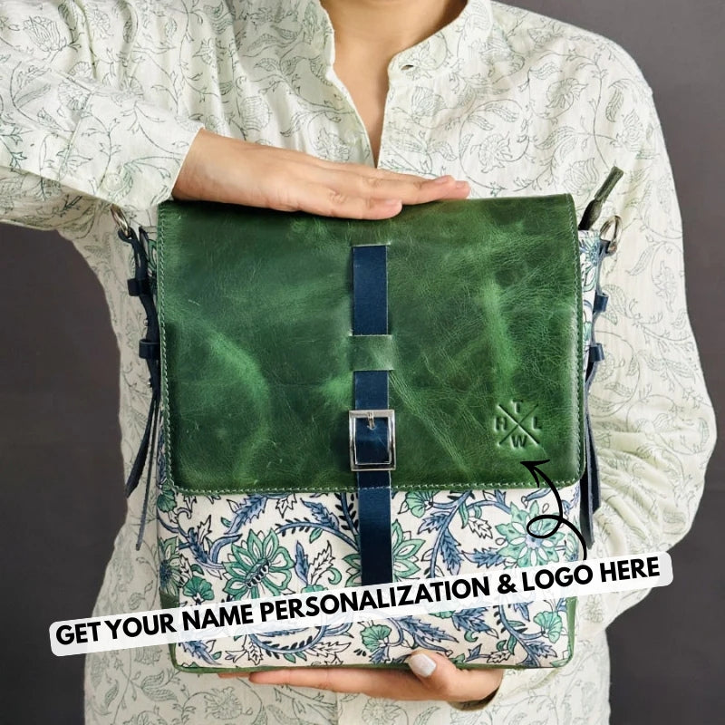 Green leather sling bag with floral pattern held by a person against a gray background