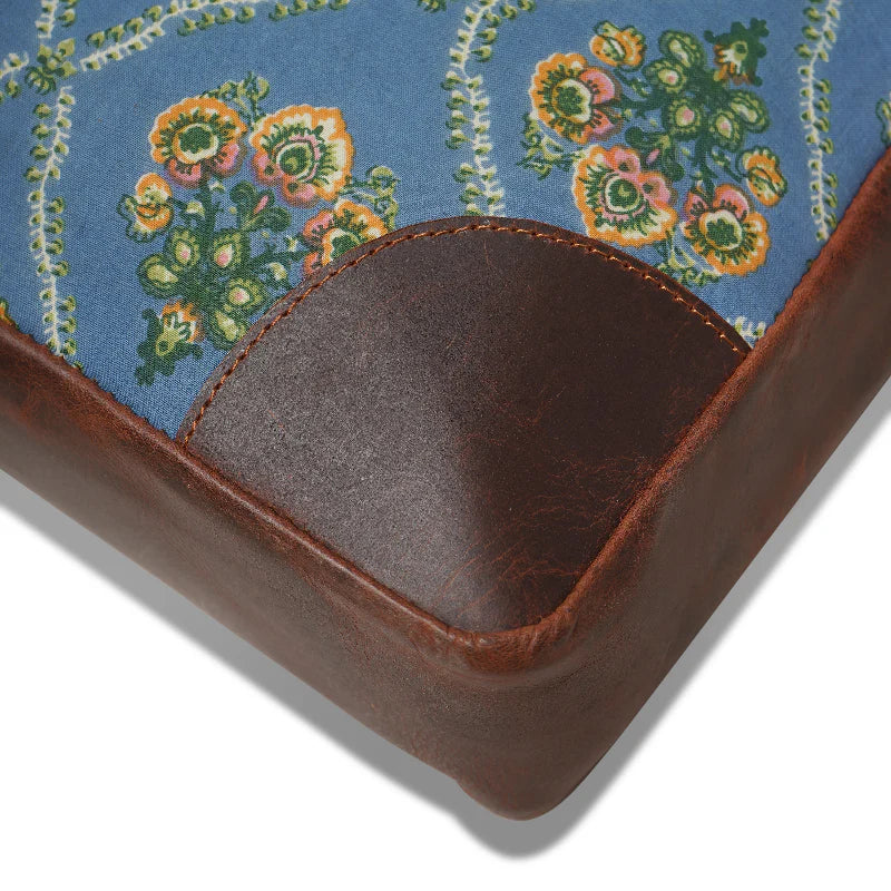 Corner of a fabric-covered product with floral pattern and brown leather trim