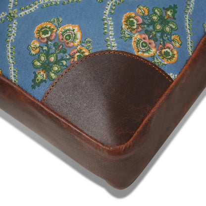Corner of a fabric-covered product with floral pattern and brown leather trim