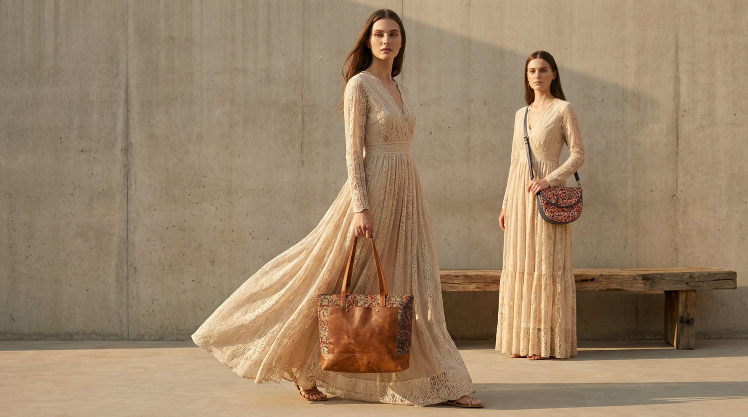 Two women in long, light-colored dresses standing against a concrete wall.