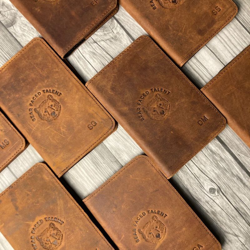Brown leather passport cover with embossed logo on a wooden surface