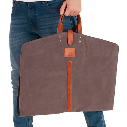 Brown garment bag with leather straps held by a person wearing blue jeans.