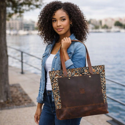 Woman holding a brown leather tote bag with floral pattern by a waterfront
