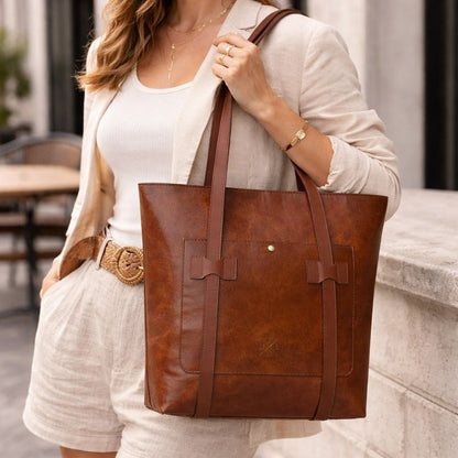 Woman holding a brown leather tote bag outdoors.