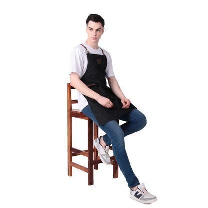 Person wearing a black apron sitting on a wooden stool against a white background
