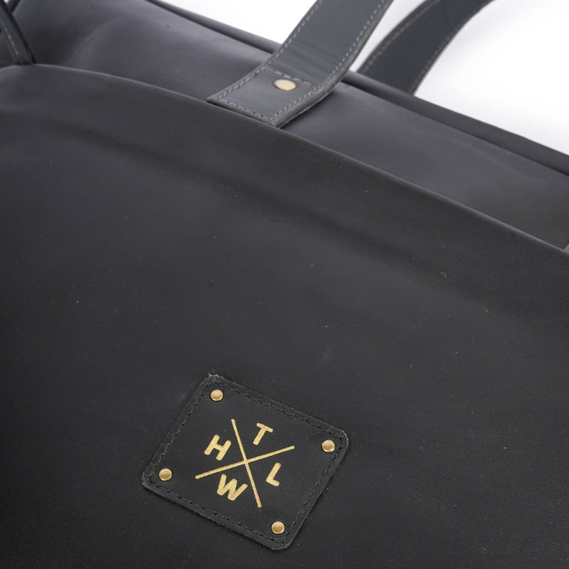 Black tote bag with gold logo and text on a white background