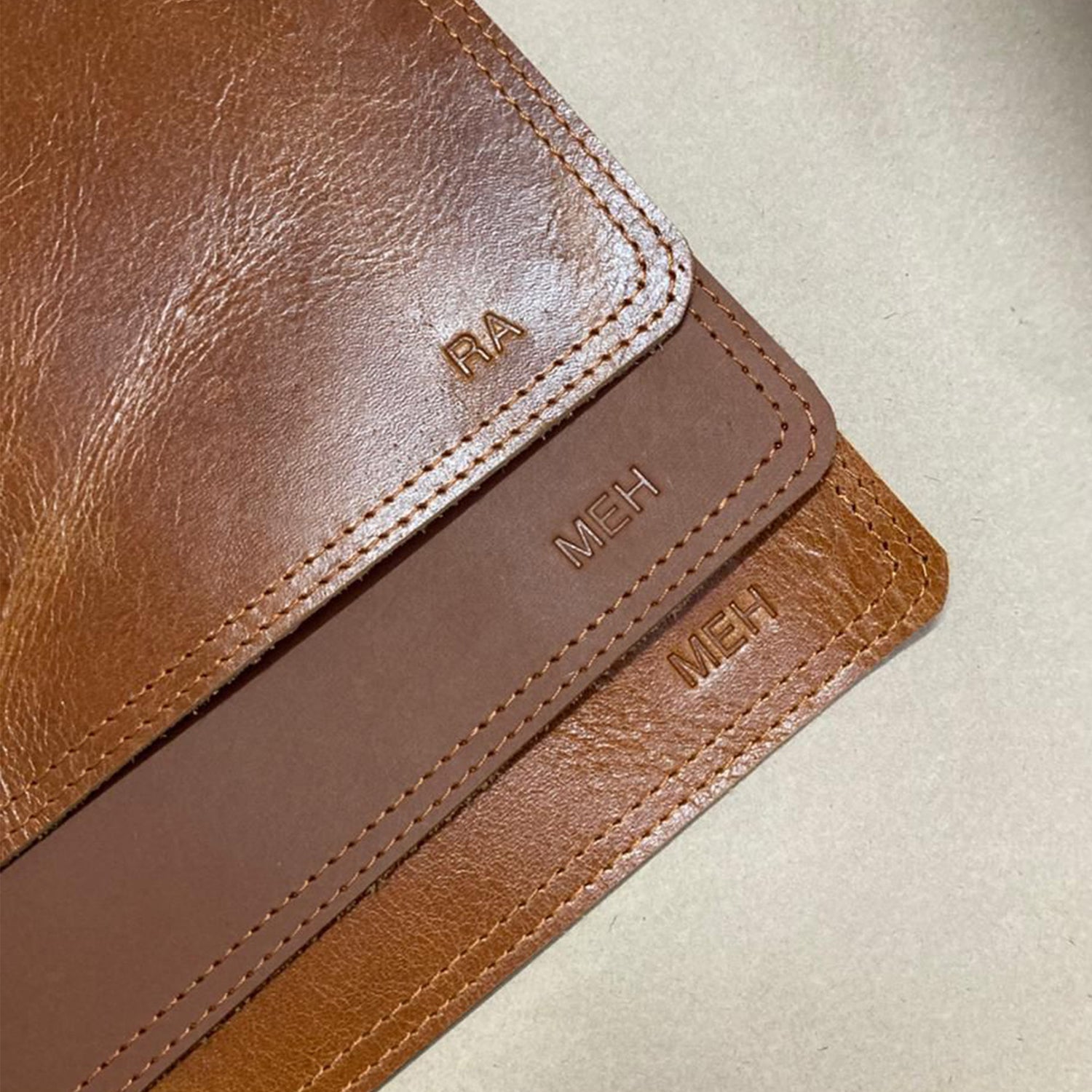 Brown leather wallet with 'RA' and 'MEH' text on a beige background