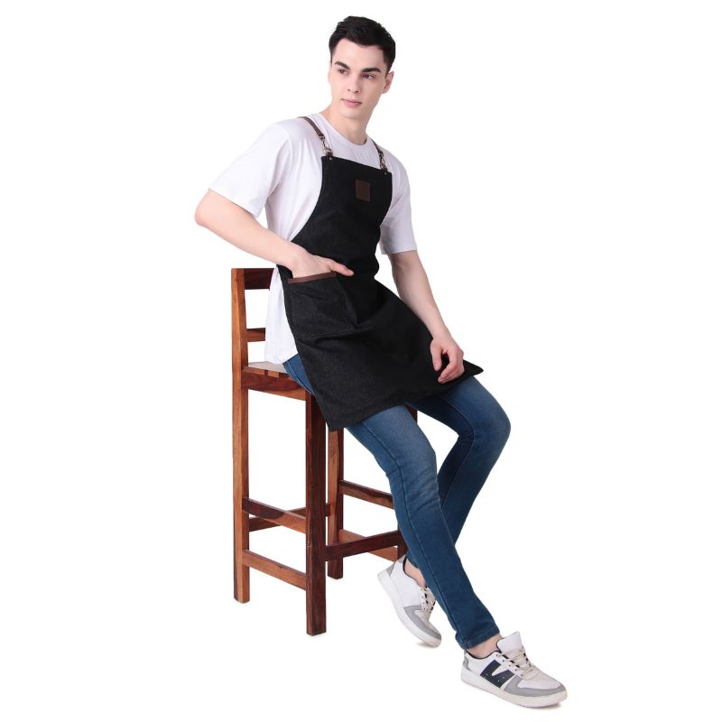 Person wearing a black apron sitting on a wooden stool against a white background