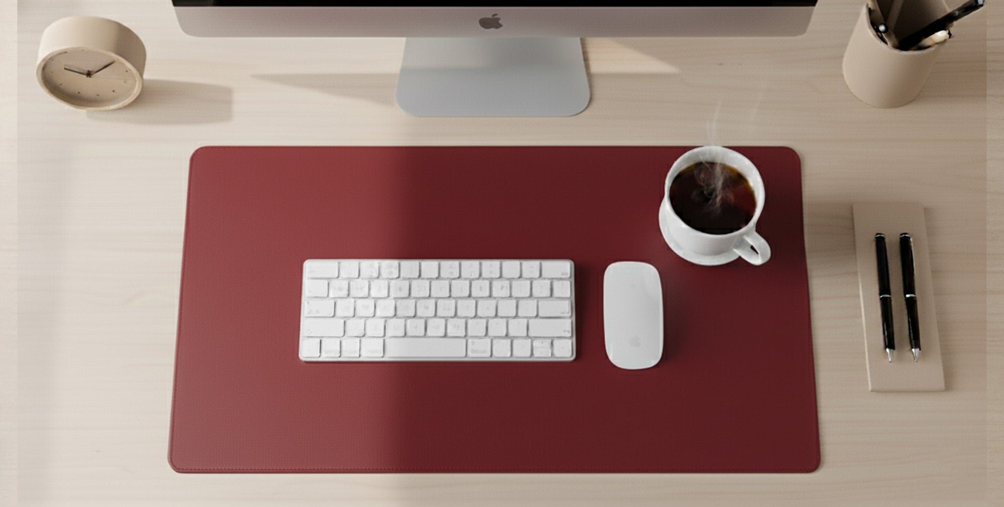 Red desk mat with a keyboard, mouse, and coffee cup on a light wooden desk.