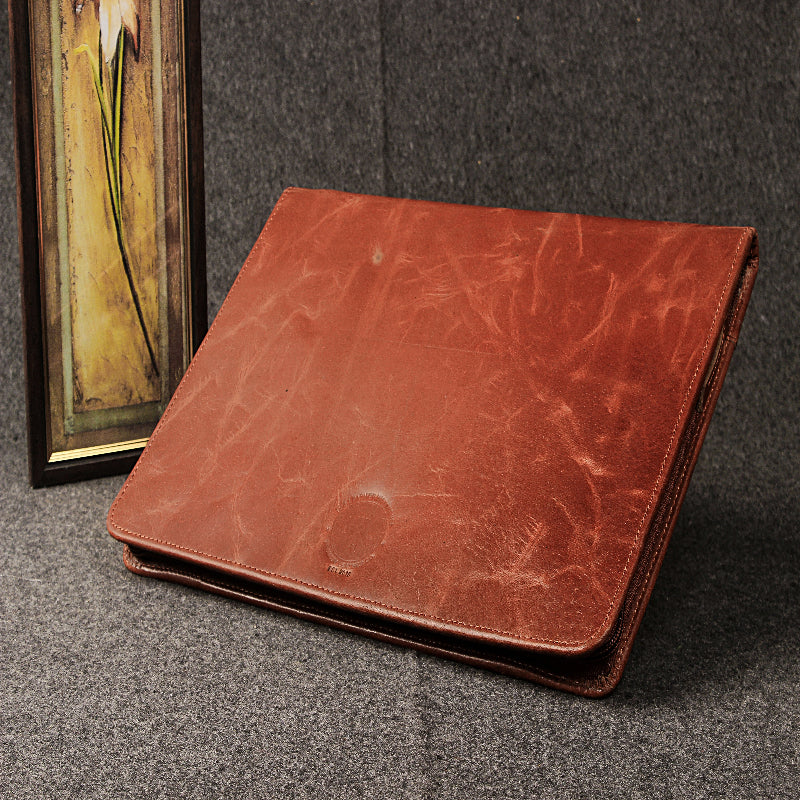 Brown leather folder on a textured surface with a framed picture in the background