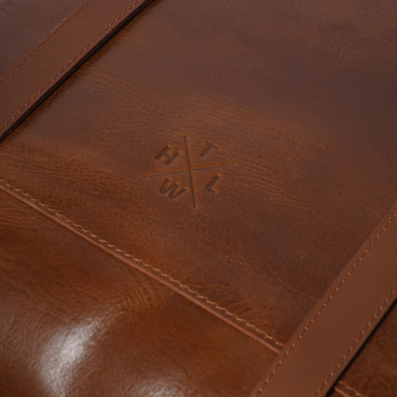 Close-up of a brown leather product with a logo, showing texture and stitching details.