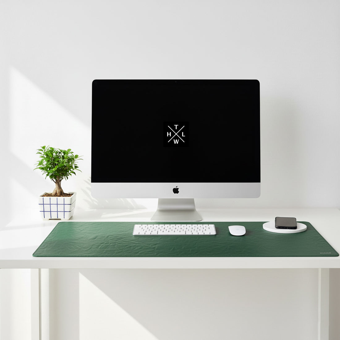 Modern desk setup with a computer monitor, keyboard, mouse, and phone on a green desk pad.