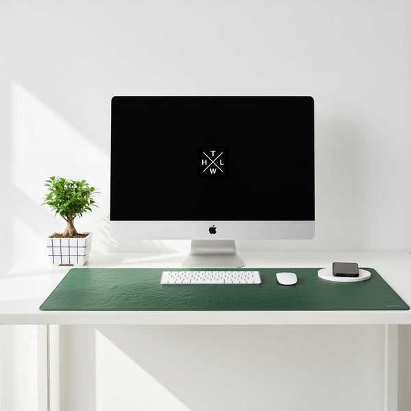 Modern desk setup with a computer monitor, keyboard, mouse, and phone on a green desk pad.