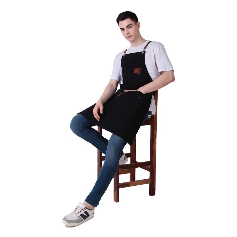 Person wearing a black apron sitting on a wooden stool against a white background