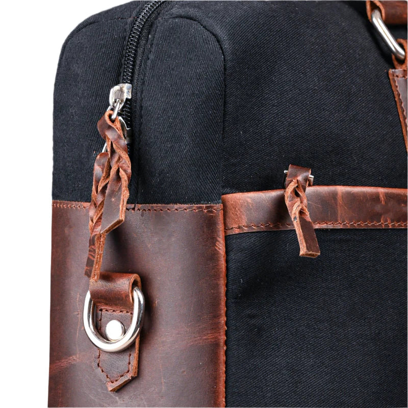 Close-up of a black bag with brown leather straps and handles.