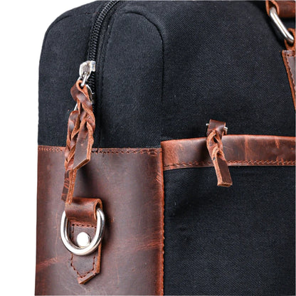 Close-up of a black bag with brown leather straps and handles.