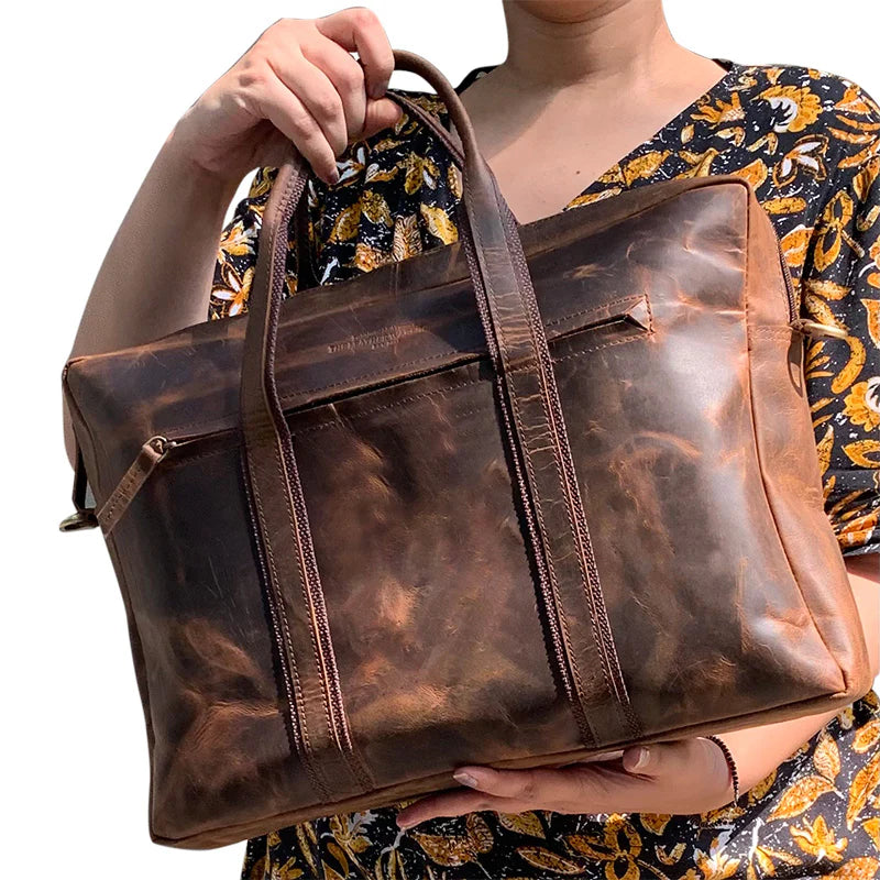 Brown leather bag held by a person wearing a floral dress.