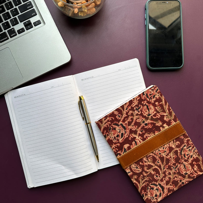 Open notebook with pen, patterned notebook, laptop, and phone on a purple surface