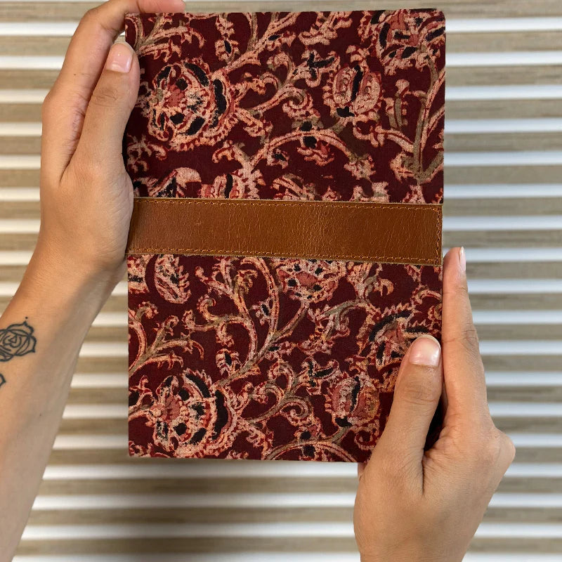 Hand holding a red patterned notebook with a brown band against a striped background