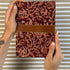 Hand holding a red patterned notebook with a brown band against a striped background