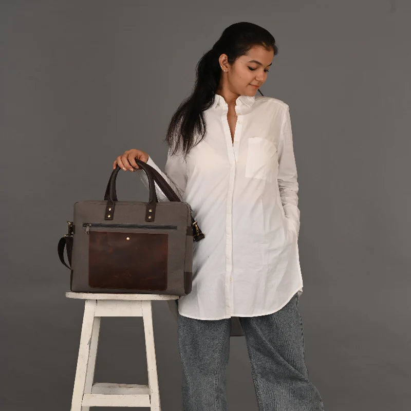 Woman holding a gray handbag with a dark brown patch on a gray background