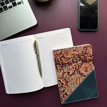 Open notebook with pen, patterned notebook, laptop, and phone on a purple surface