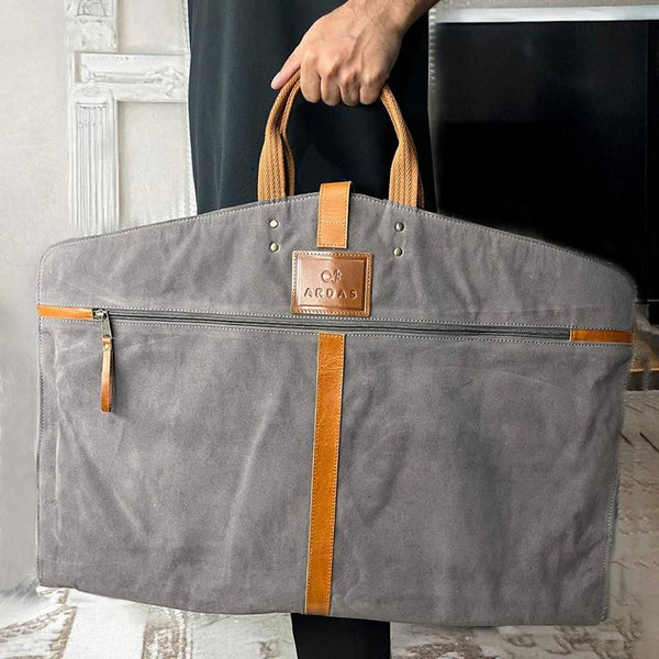 Gray  garmen bag with brown accents held by a person indoors