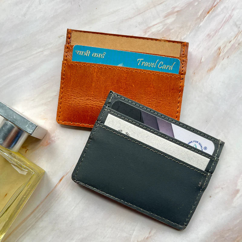 Two leather card holders, one brown and one black, on a light marble surface.