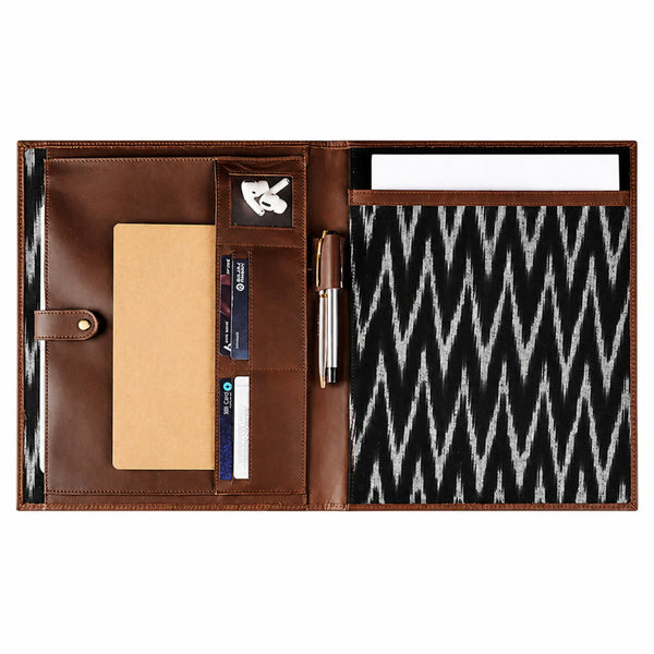 An open brown leather organizer case with multiple compartments, a card holder, a pen slot, a notebook, and a black-and-white ikat patterned insert, shown on a white background.