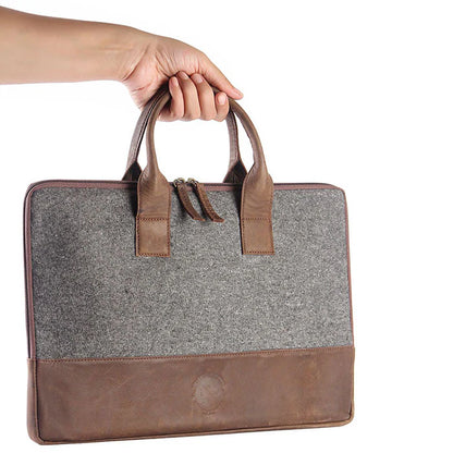 Gray briefcase with brown leather accents held by a hand on a white background