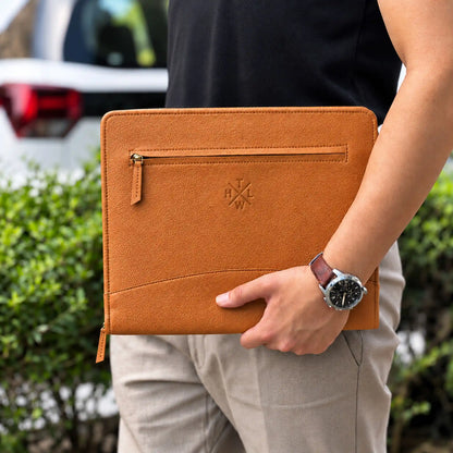 Person carrying a tan leather portfolio with an exterior zipper pocket and wristwatch