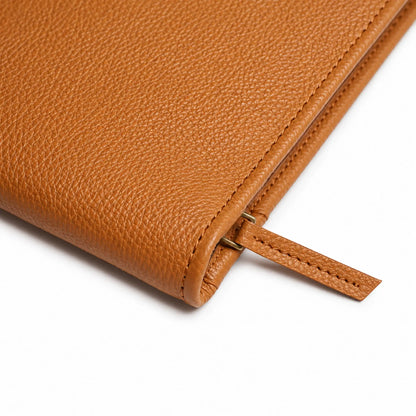 Close-up of textured tan leather, reinforced stitching, and zipper pull detail on a portfolio