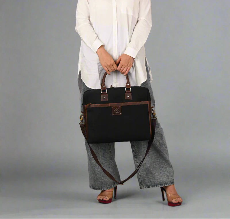 Person holding a black handbag with brown straps on a gray background