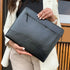 Person holding a black leather clutch bag outdoors