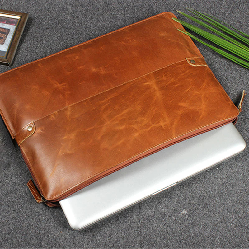 Brown leather laptop sleeve on a gray surface with a plant in the background